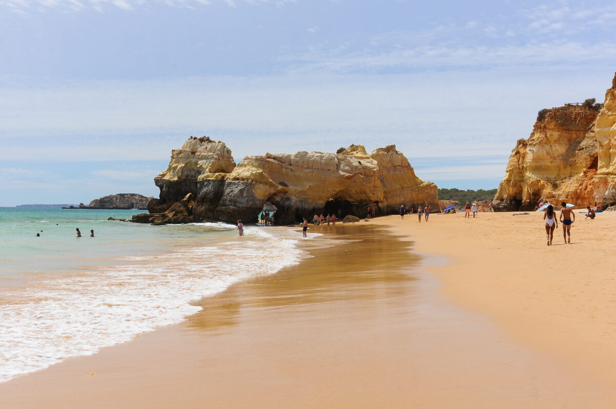 Golden sand beach framed by large, jagged sandstone rock formations in the Algarve, Portugal.