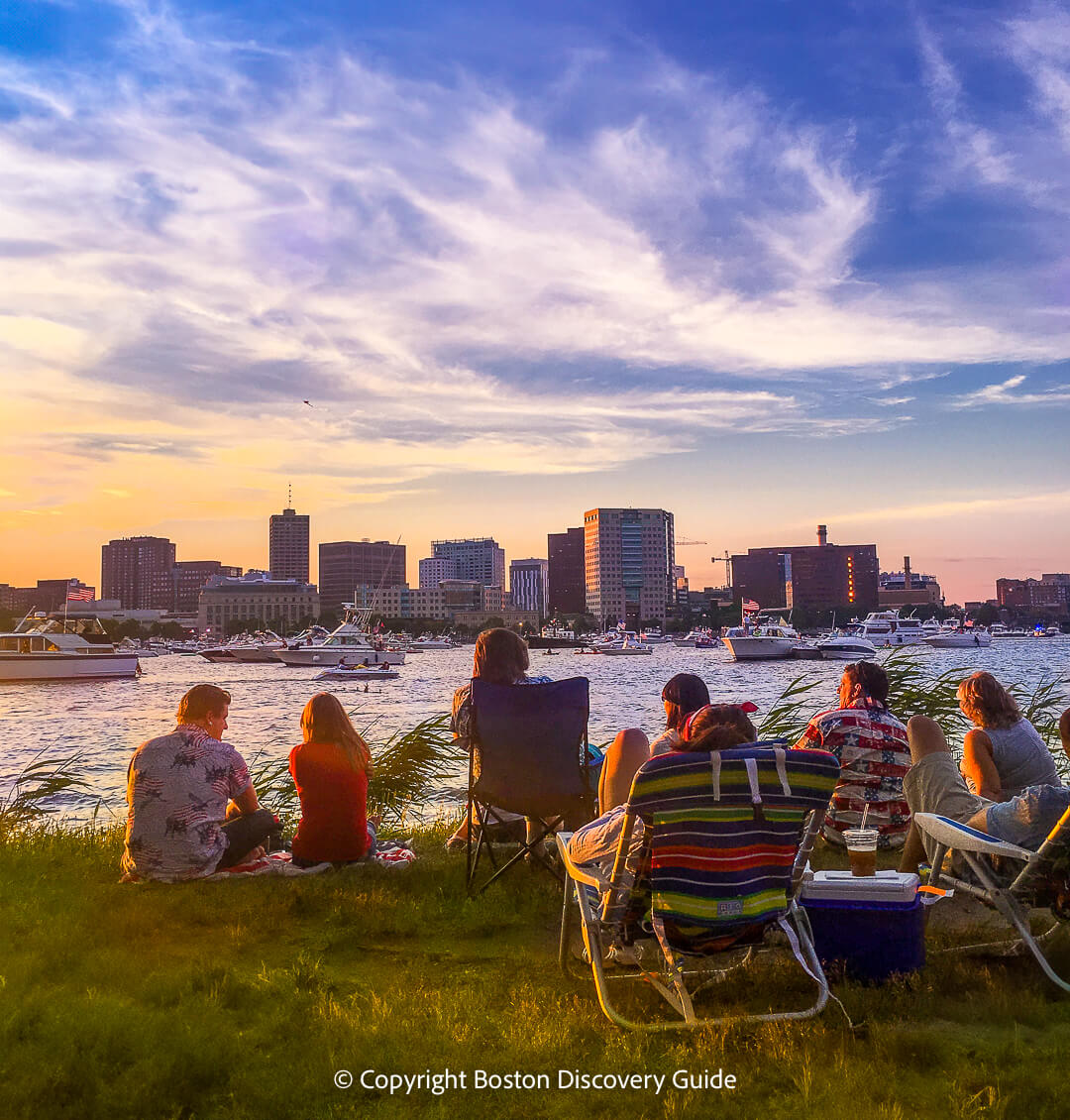 People sitting on the grass along the river bank with coolers and chairs waiting for the sunset.