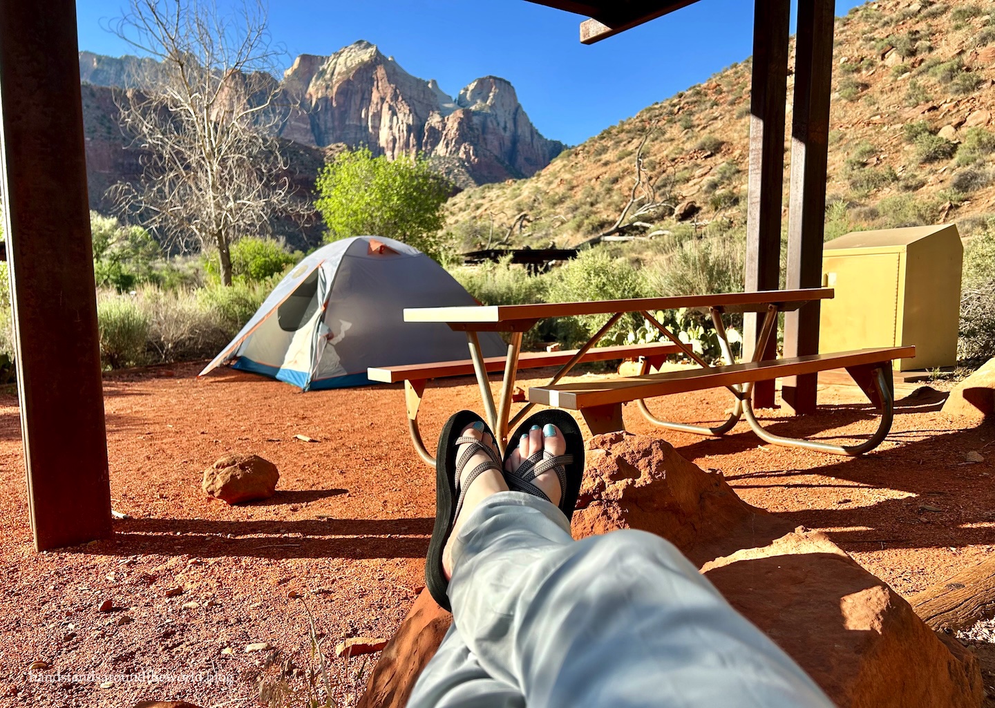 A glowing tent at Watchman Campground at twilight with mountain silhouettes in the background.