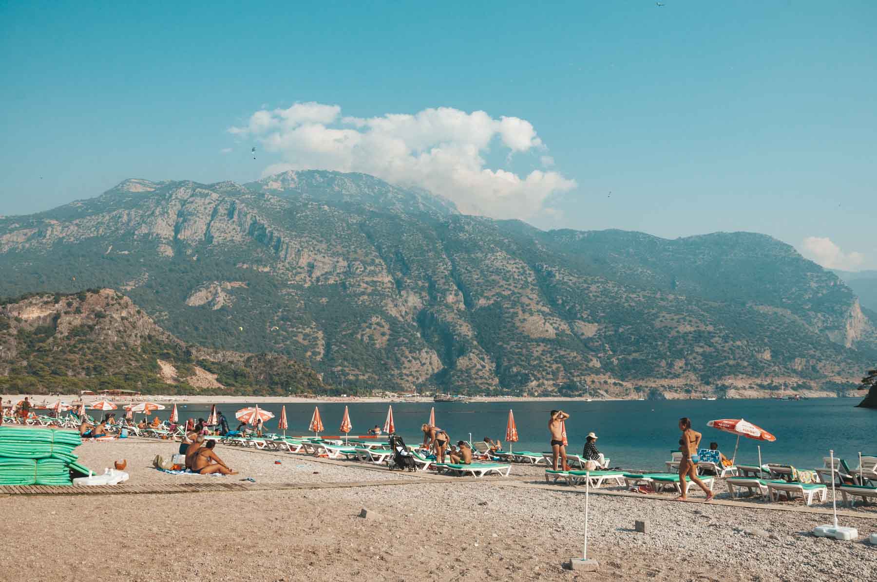 A vibrant beach scene in Ölüdeniz featuring clear blue water and paragliders in the sky.