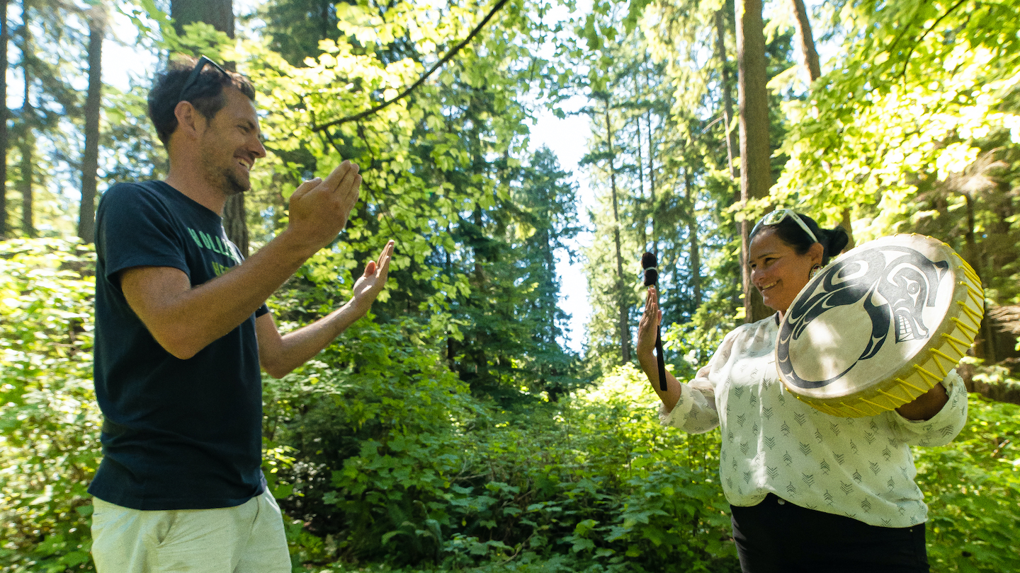 A guide explaining local plant life to a visitor in a forested park setting.