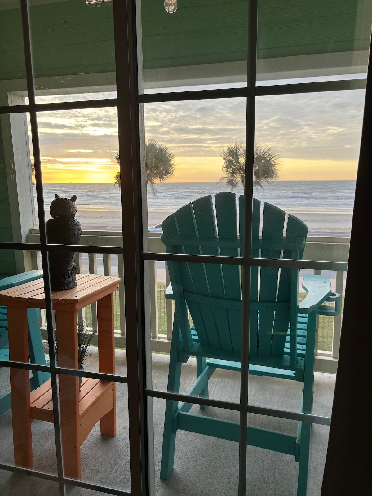Two Adirondack chairs on a balcony overlooking the ocean at sunrise.