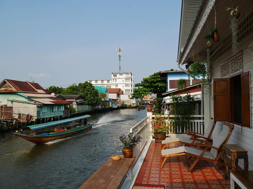 A peaceful wooden terrace of a traditional Thai house overlooking a quiet canal.