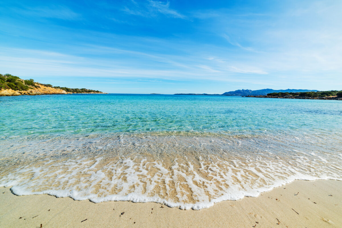 Vibrant blue and turquoise water washing onto a white sand beach at Spiaggia del Relitto.