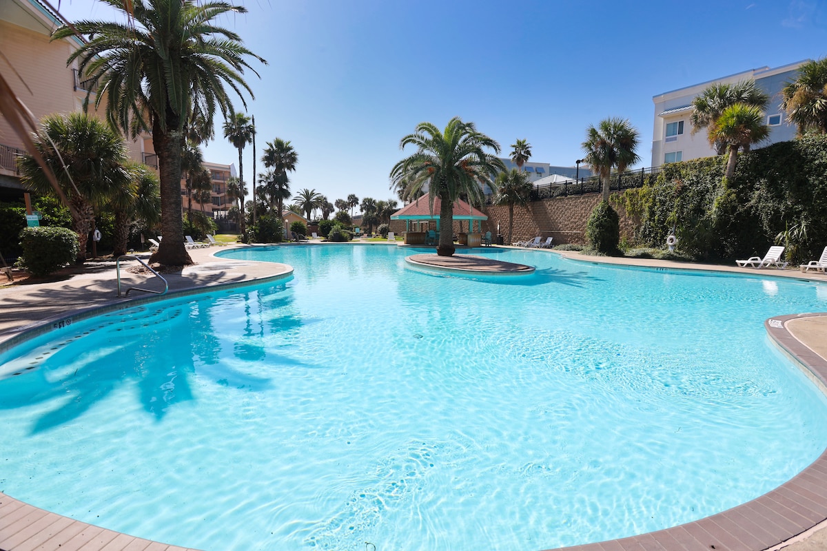 A large outdoor resort swimming pool surrounded by tropical palm trees.