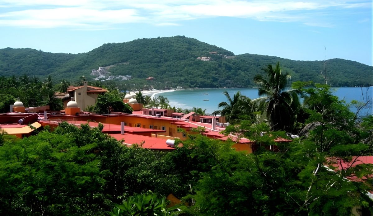 Aerial view of red-roofed buildings nestled in tropical greenery overlooking Playa La Ropa in Zihuatanejo.