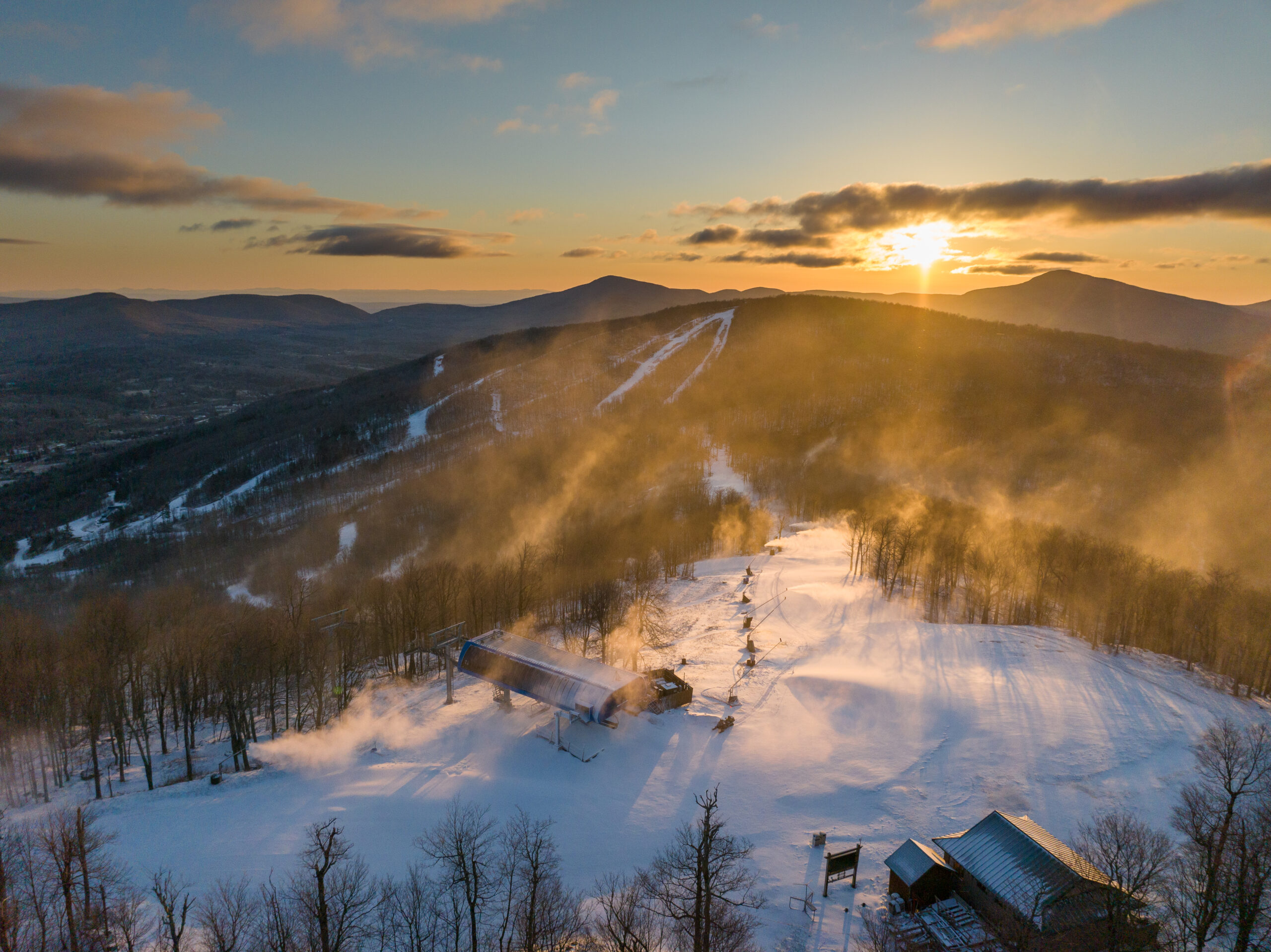 Snowy ski slopes at Windham Mountain under a bright sky with mountain peaks in the background.