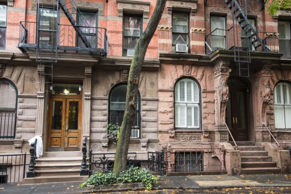 A row of historic red brick townhouses with iron railings and green trees.