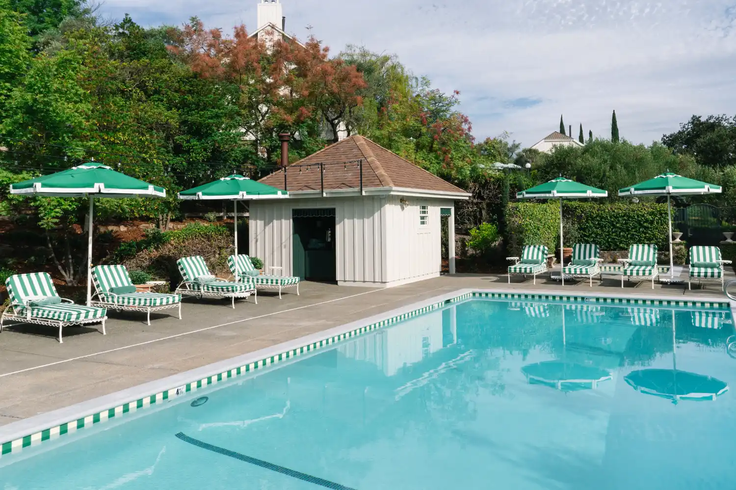 A luxury swimming pool area with green-striped umbrellas and lounge chairs.