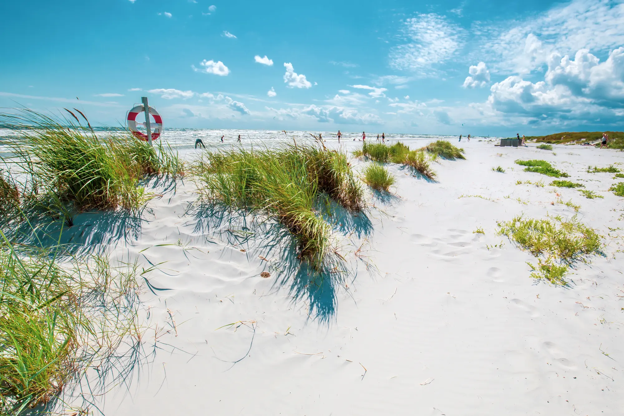 Vast white sand dunes with a distant red and white life saver ring under a clear sky on Bornholm island.