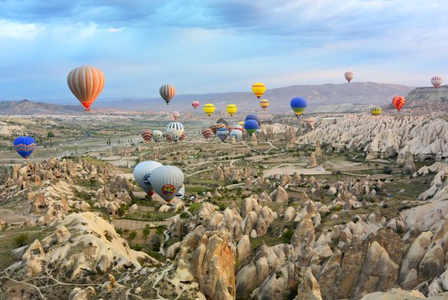 Dozens of colorful hot air balloons floating over the rocky valleys of Cappadocia at sunrise.