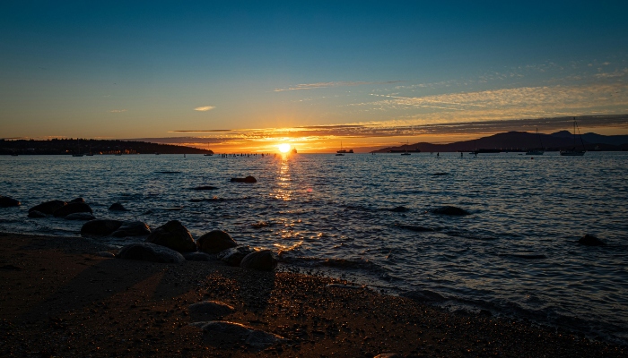 The sun setting over the ocean and mountains at Kitsilano Beach in Vancouver.