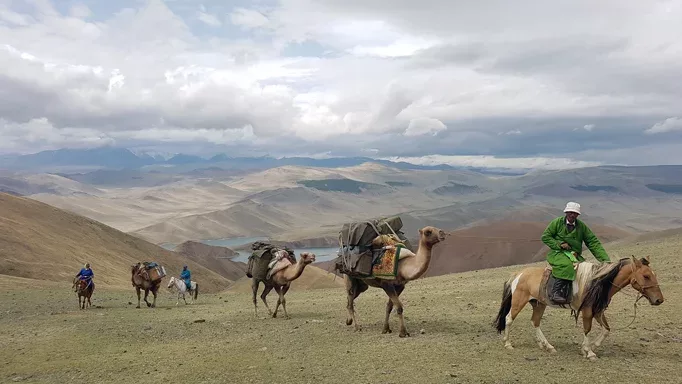 Nomadic herders leading a caravan of camels through the rugged terrain of Western Mongolia.