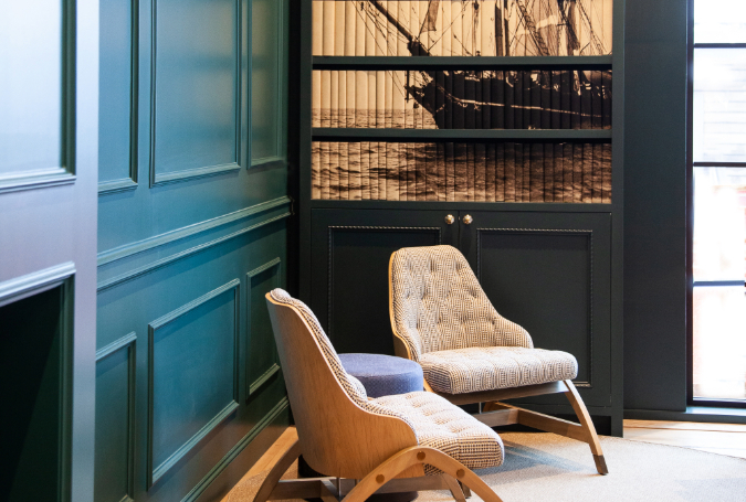 A cozy corner of a boutique hotel room with a blue velvet chair and a curated bookshelf.