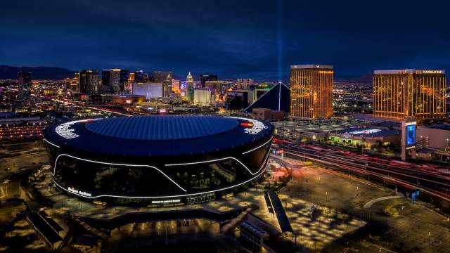 Aerial night view of Allegiant Stadium with the glowing lights of the Las Vegas Strip in the distance.