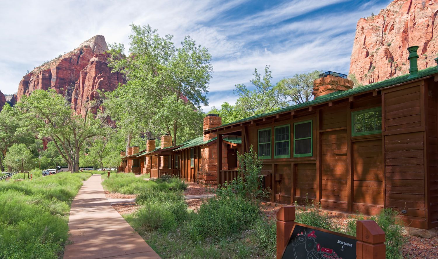 The exterior of the Zion Lodge surrounded by tall trees and red rock cliffs.
