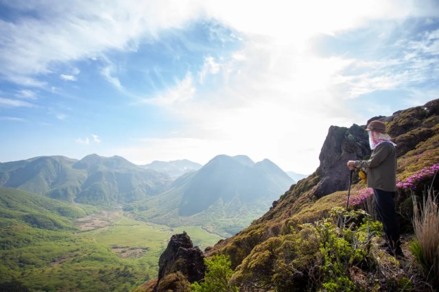 A lone hiker with a backpack standing on a ridge looking out over a deep mountain valley.