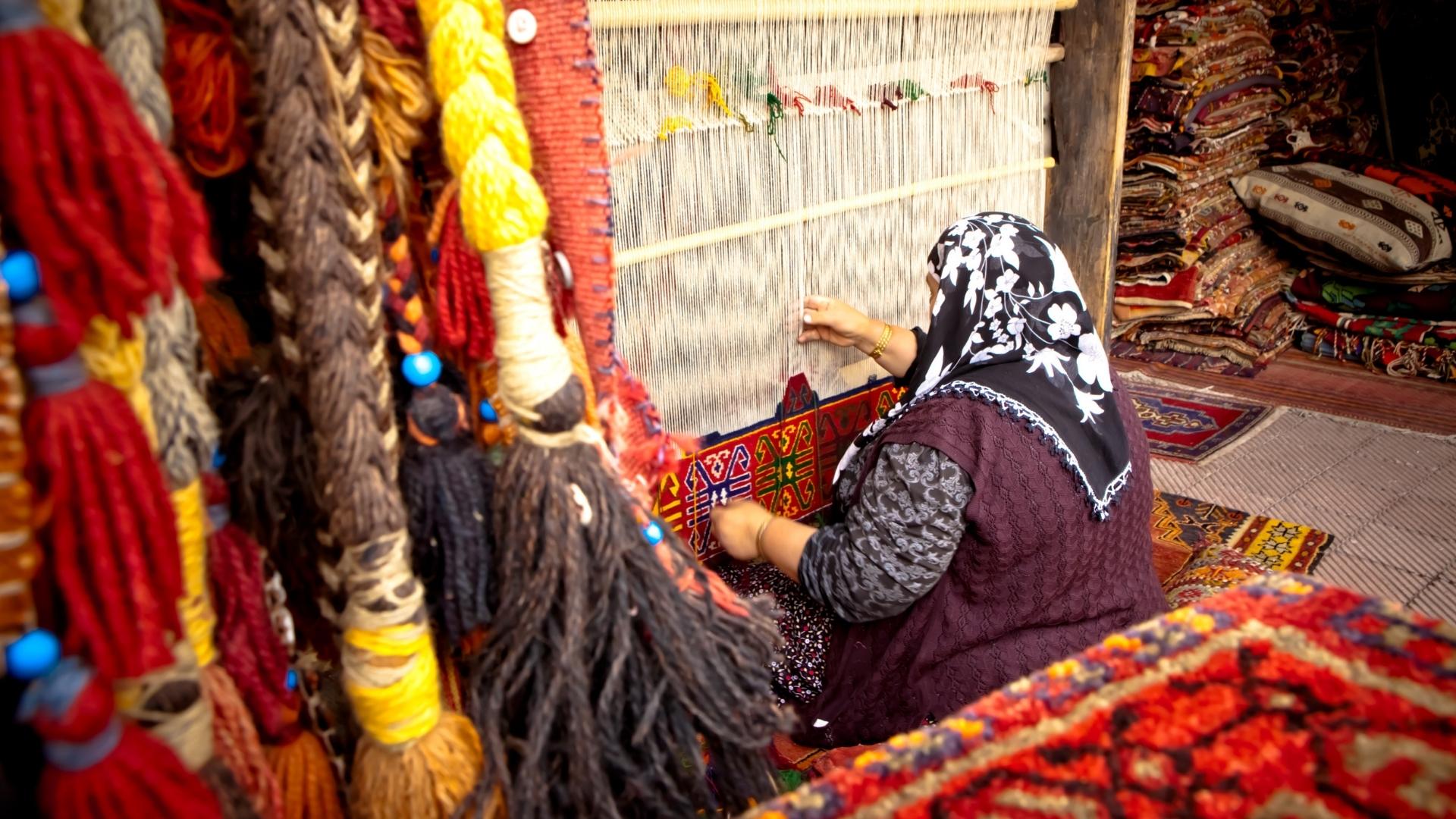Stacks of colorful hand-woven Turkish carpets and textiles in an artisan shop.