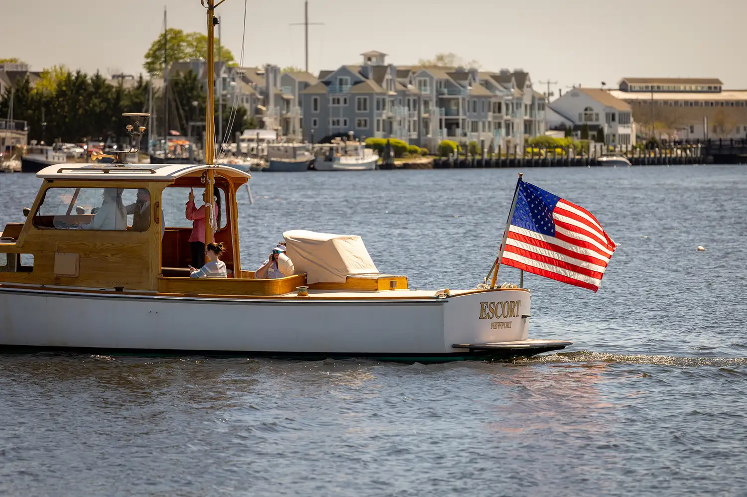 A classic motorboat with an American flag cruising on the Mystic River near the shore.