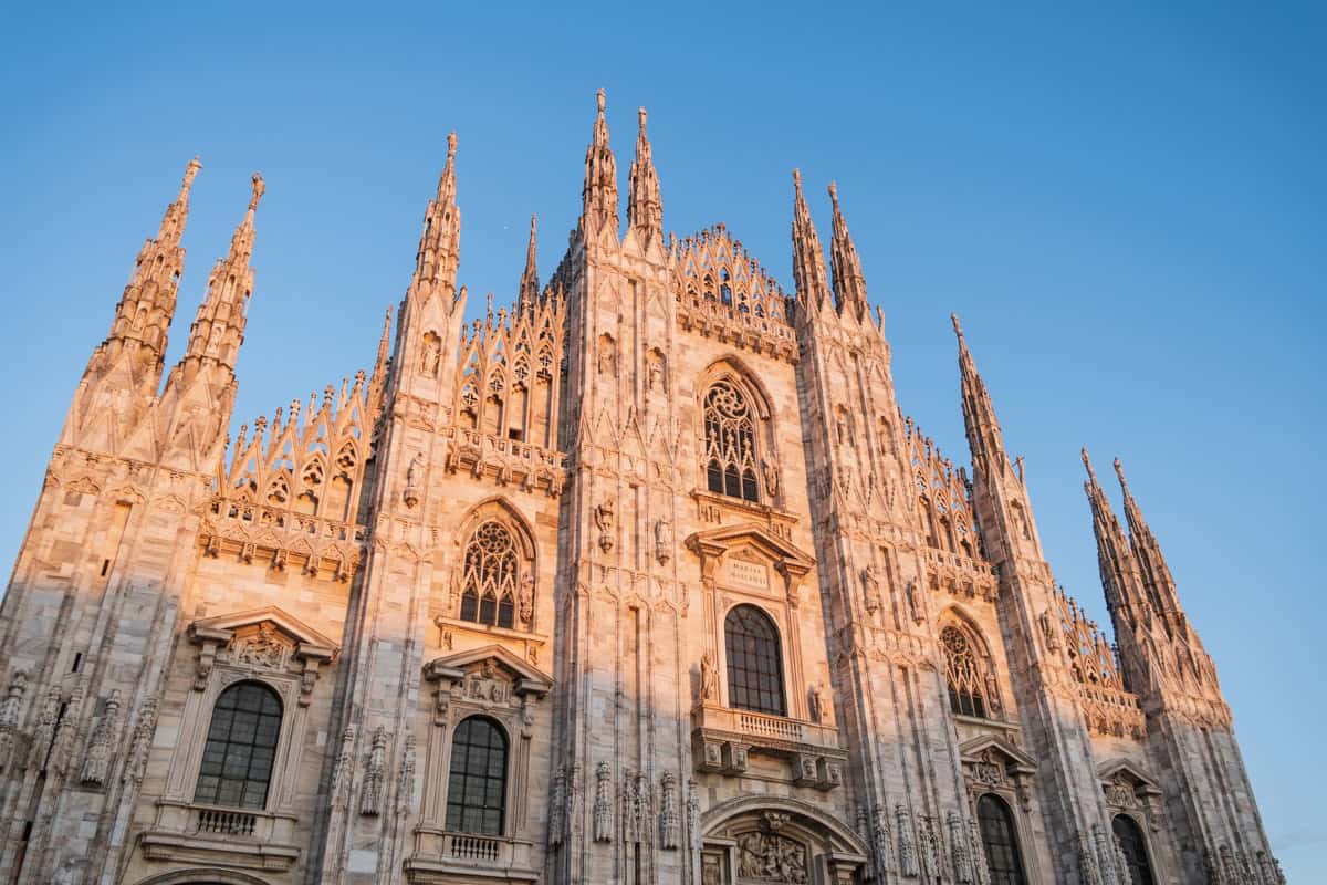 The Gothic-style Duomo di Milano cathedral during sunset with golden light hitting the facade.