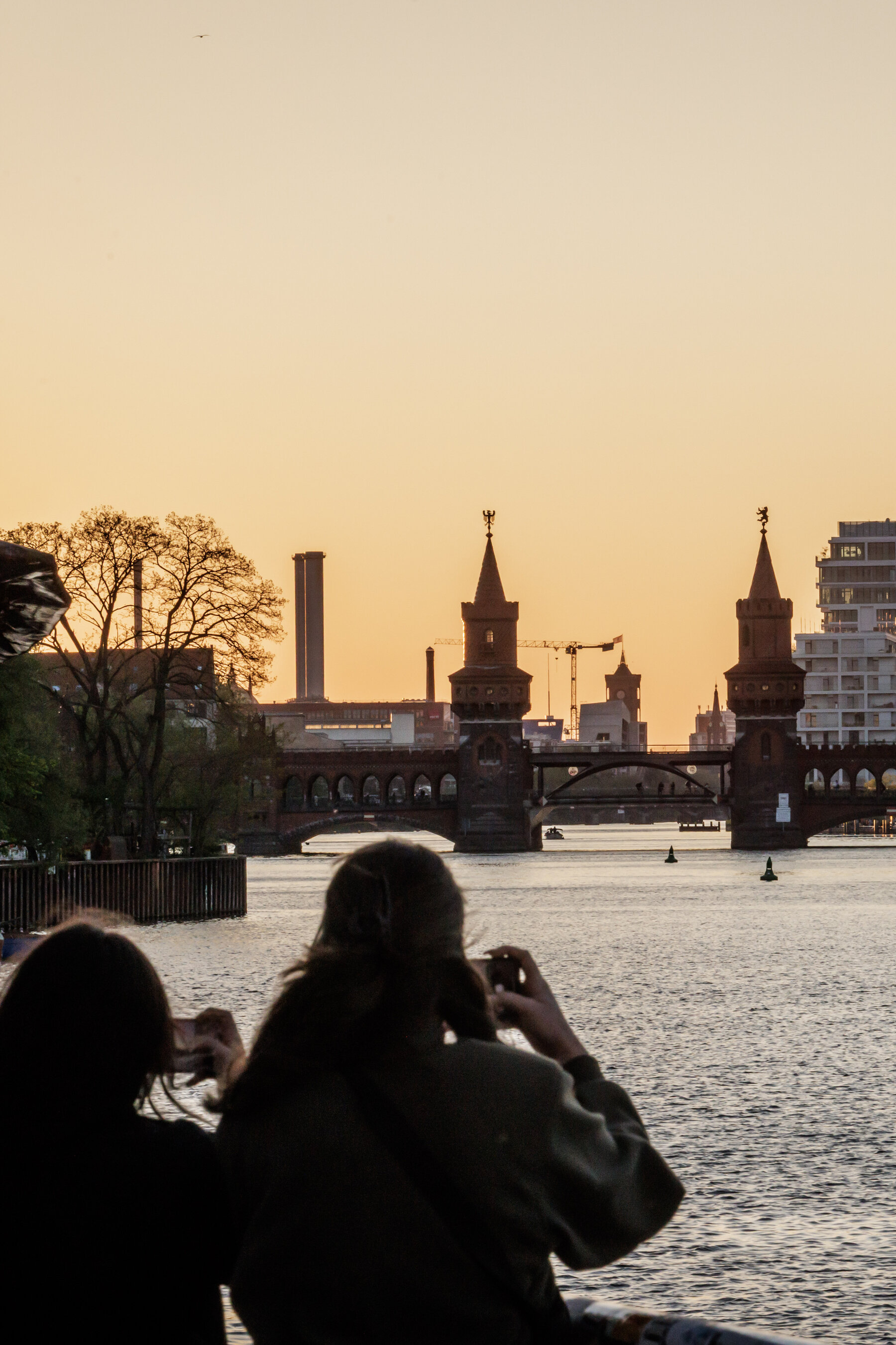 The iconic brick Oberbaum Bridge stretching over the Spree River at sunset with the Berlin skyline in the distance.