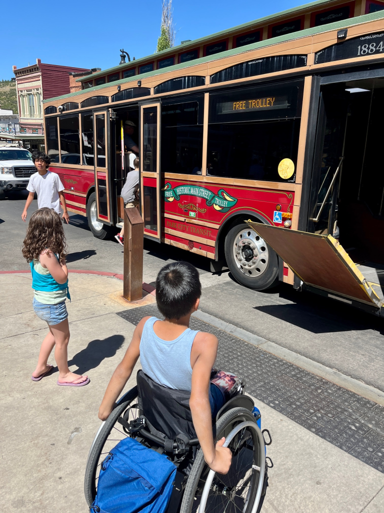 A red historic-style trolley in Park City with a mechanical wheelchair ramp extended to the sidewalk.