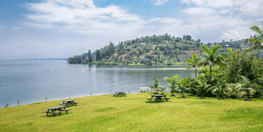 A luxury resort terrace with wooden furniture overlooking the calm blue waters and hills of Lake Kivu.