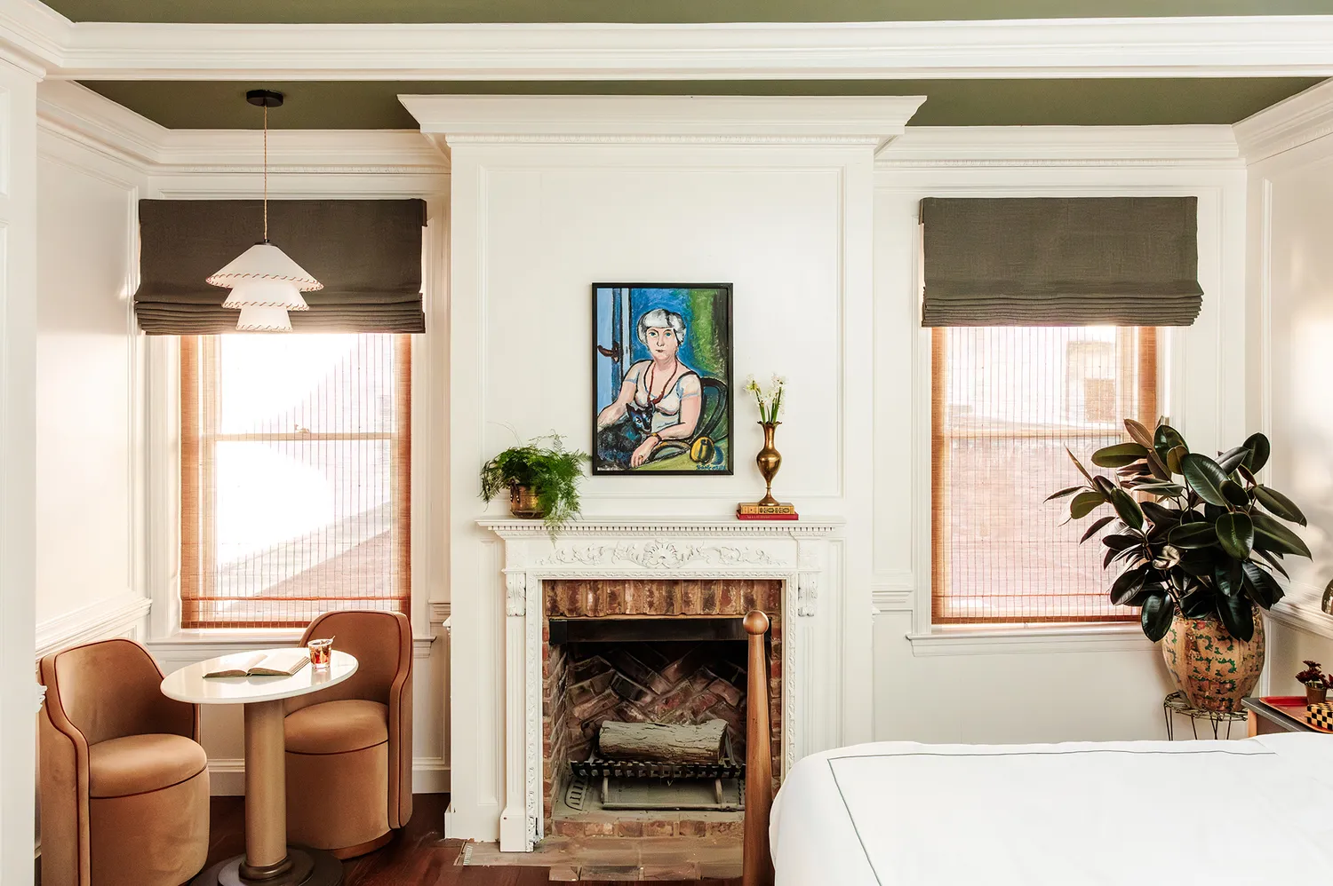 A guest room at The Chloe Nashville featuring a vintage fireplace, local artwork, and a plush bed with indoor plants.