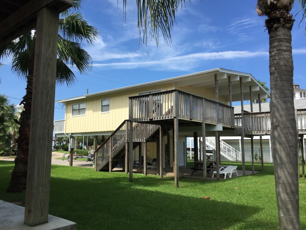 A bright yellow two-story coastal cottage with palm trees and a boat dock.