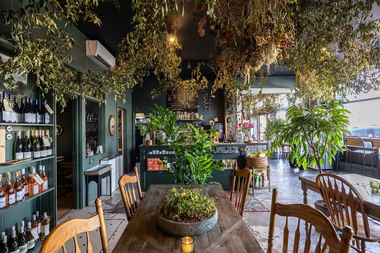 A cozy cafe interior at Flora with rustic wooden furniture and lush plants hanging from the ceiling.