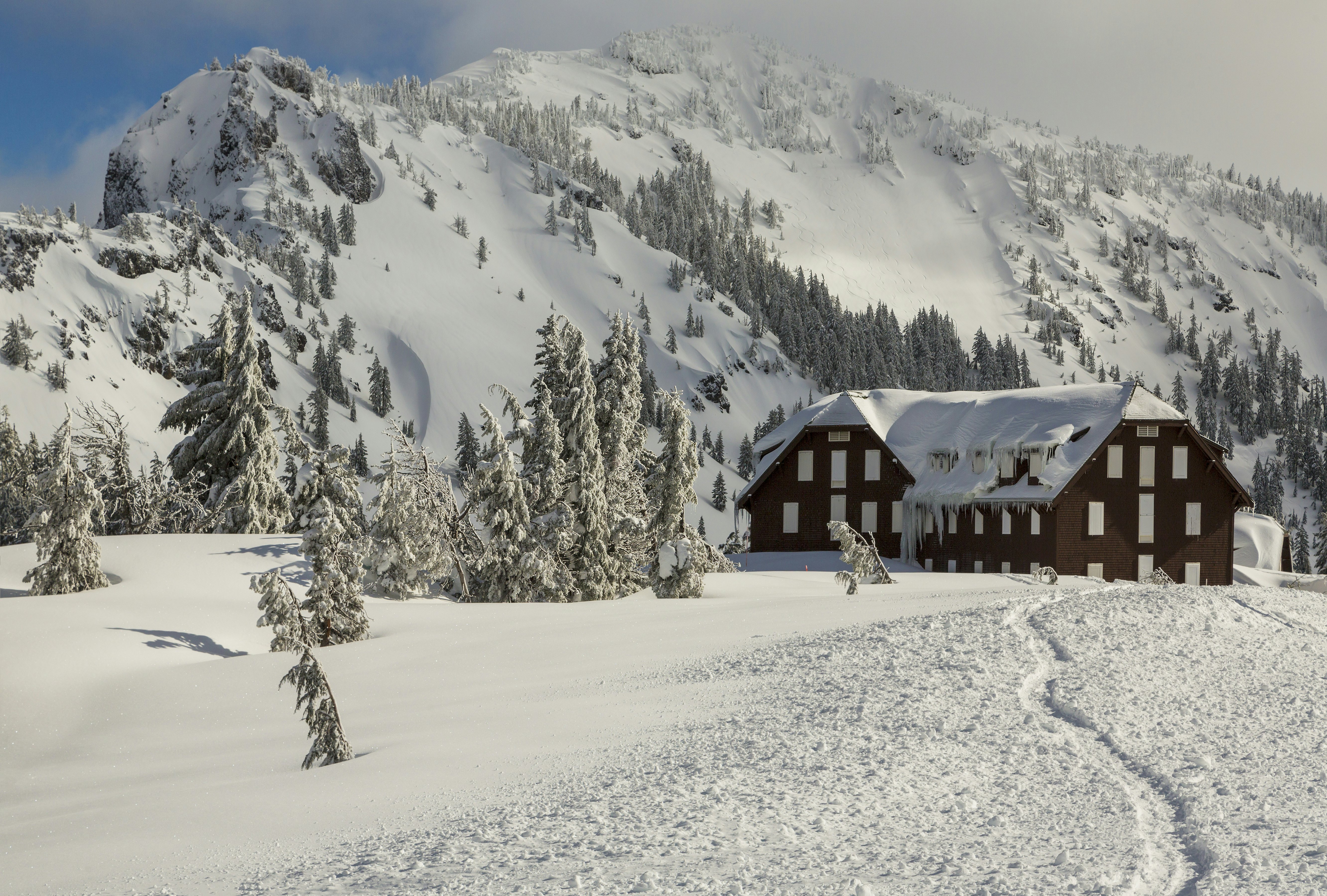 The stone and wood exterior of Crater Lake Lodge heavily draped in winter snow.