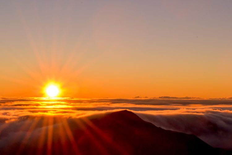 The sun rising over the clouds and volcanic landscape at the summit of Haleakalā.