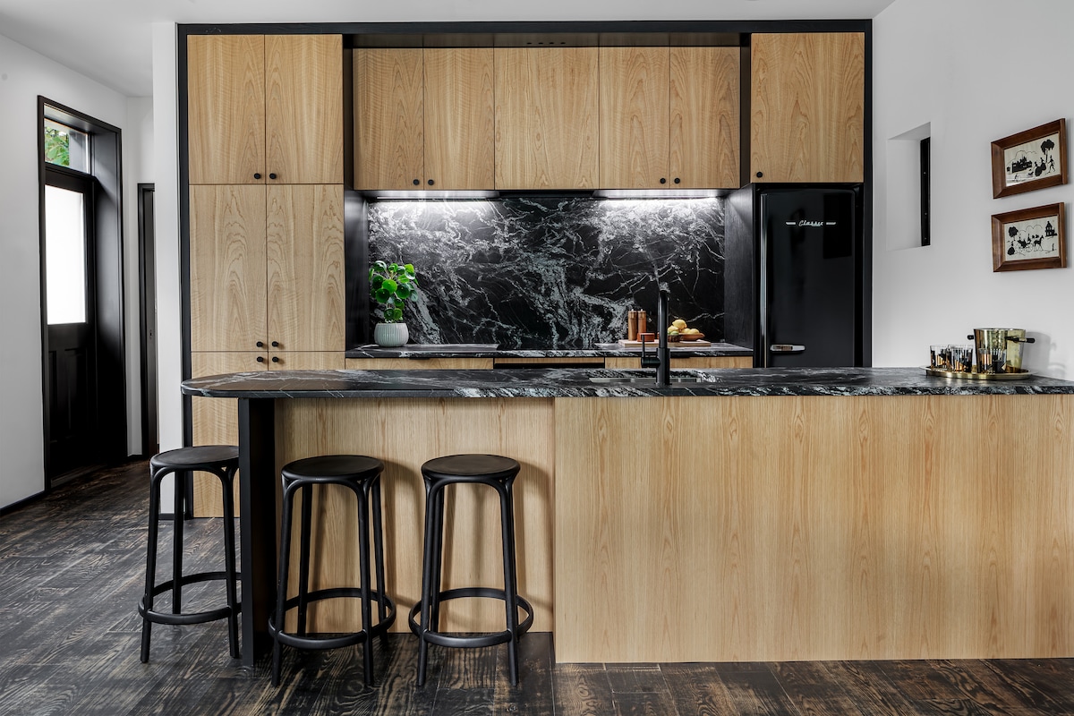 A high-end kitchen with black marble countertops, sleek wood cabinets, and modern lighting.