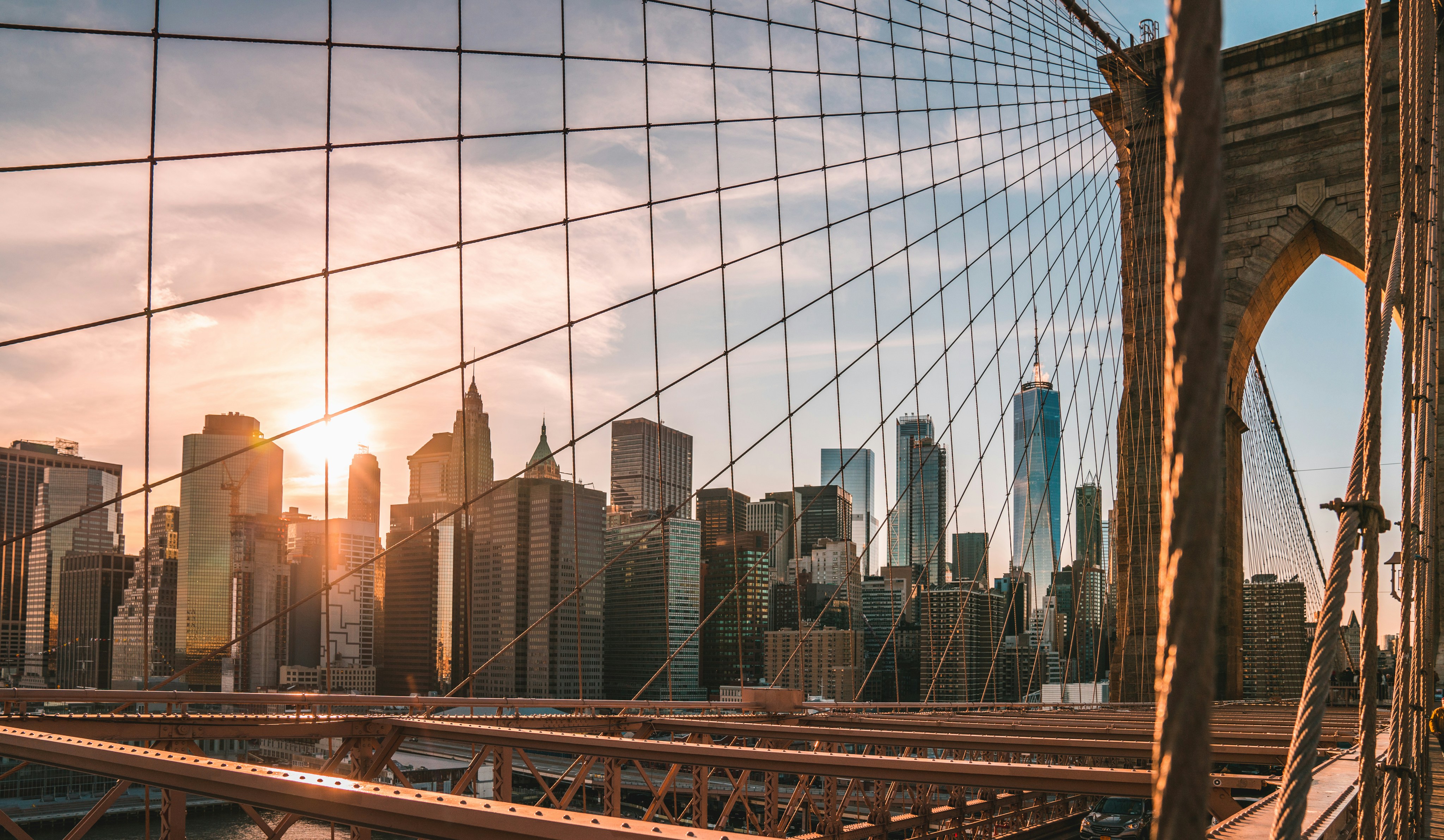 The suspension cables and stone arches of the Brooklyn Bridge against a bright sky.
