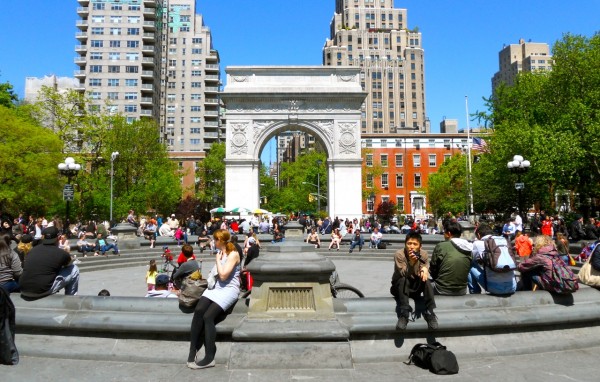 The white marble Washington Square Arch with trees and the park fountain in the background.