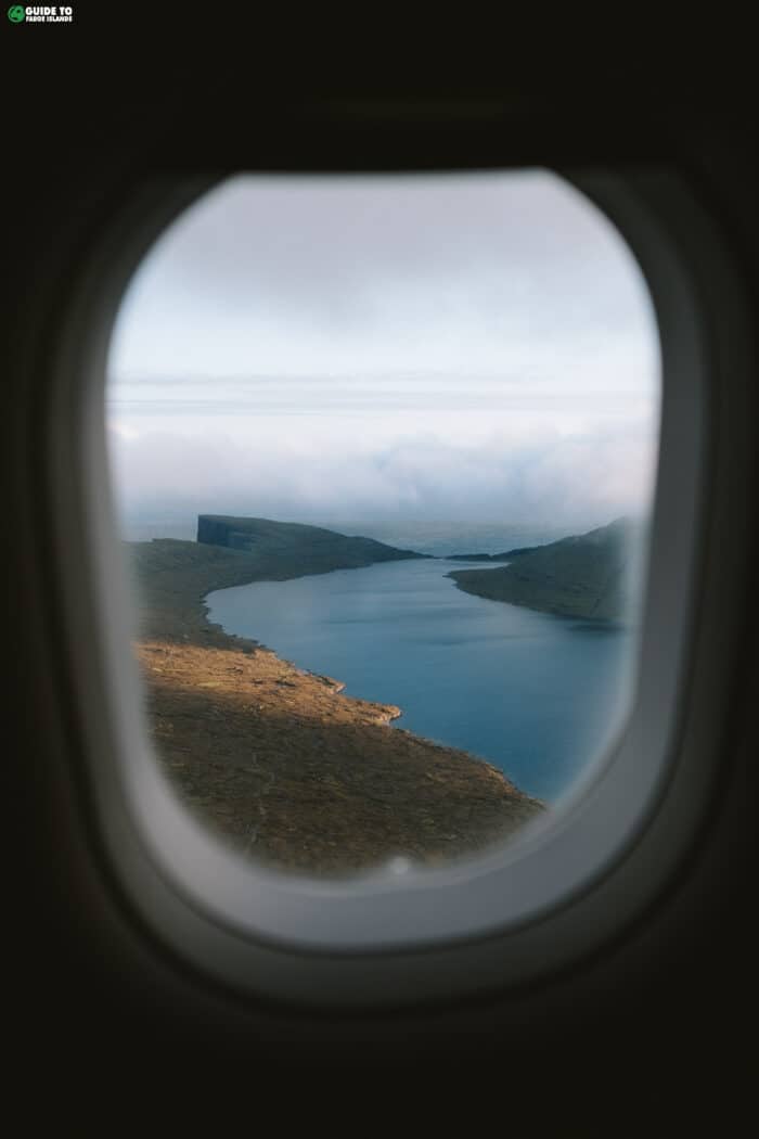 The wing of an airplane and the rugged islands of the Faroes seen through a flight window.