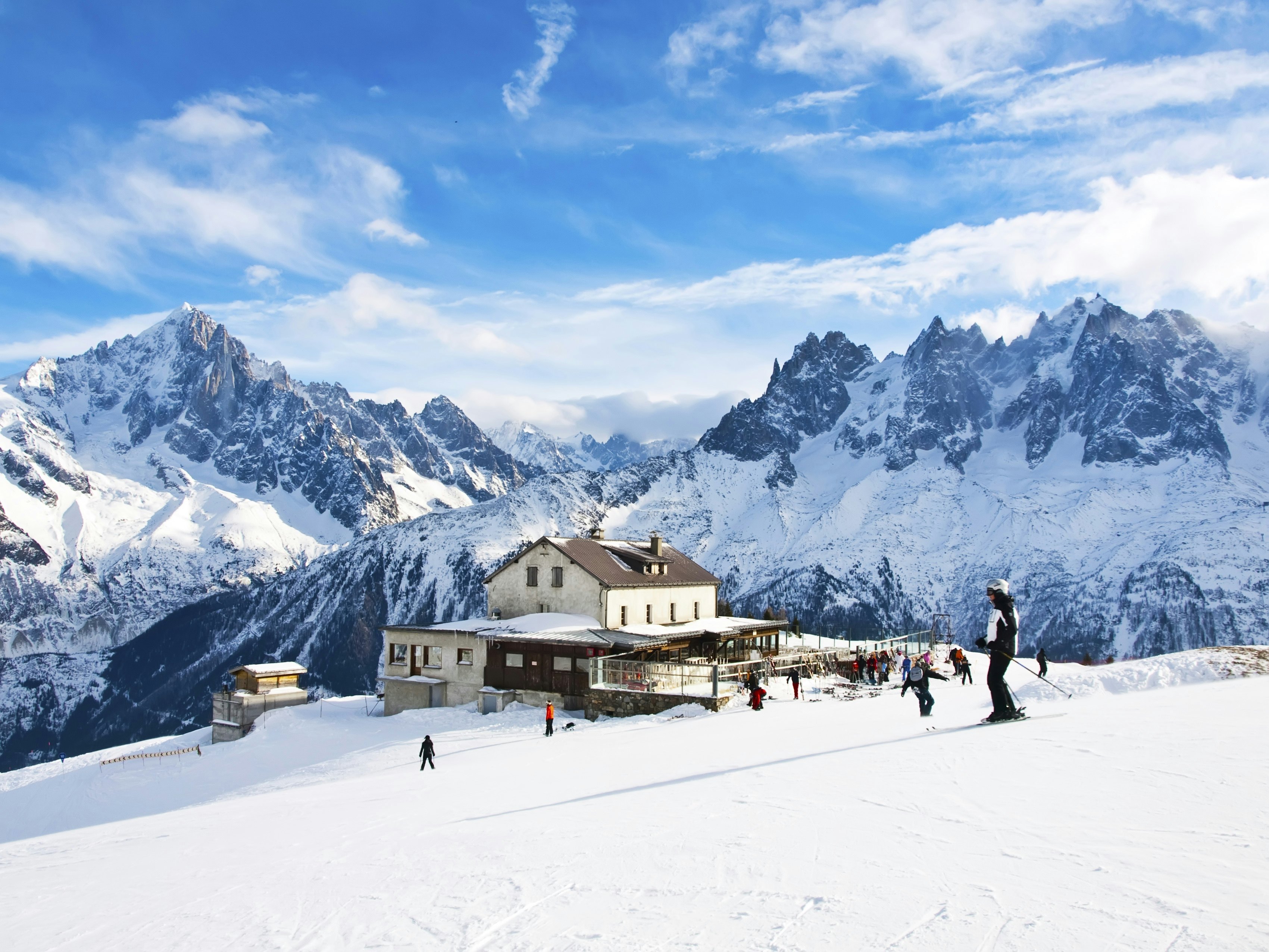 Skiers gliding past a luxury mountain lodge in a French ski resort.