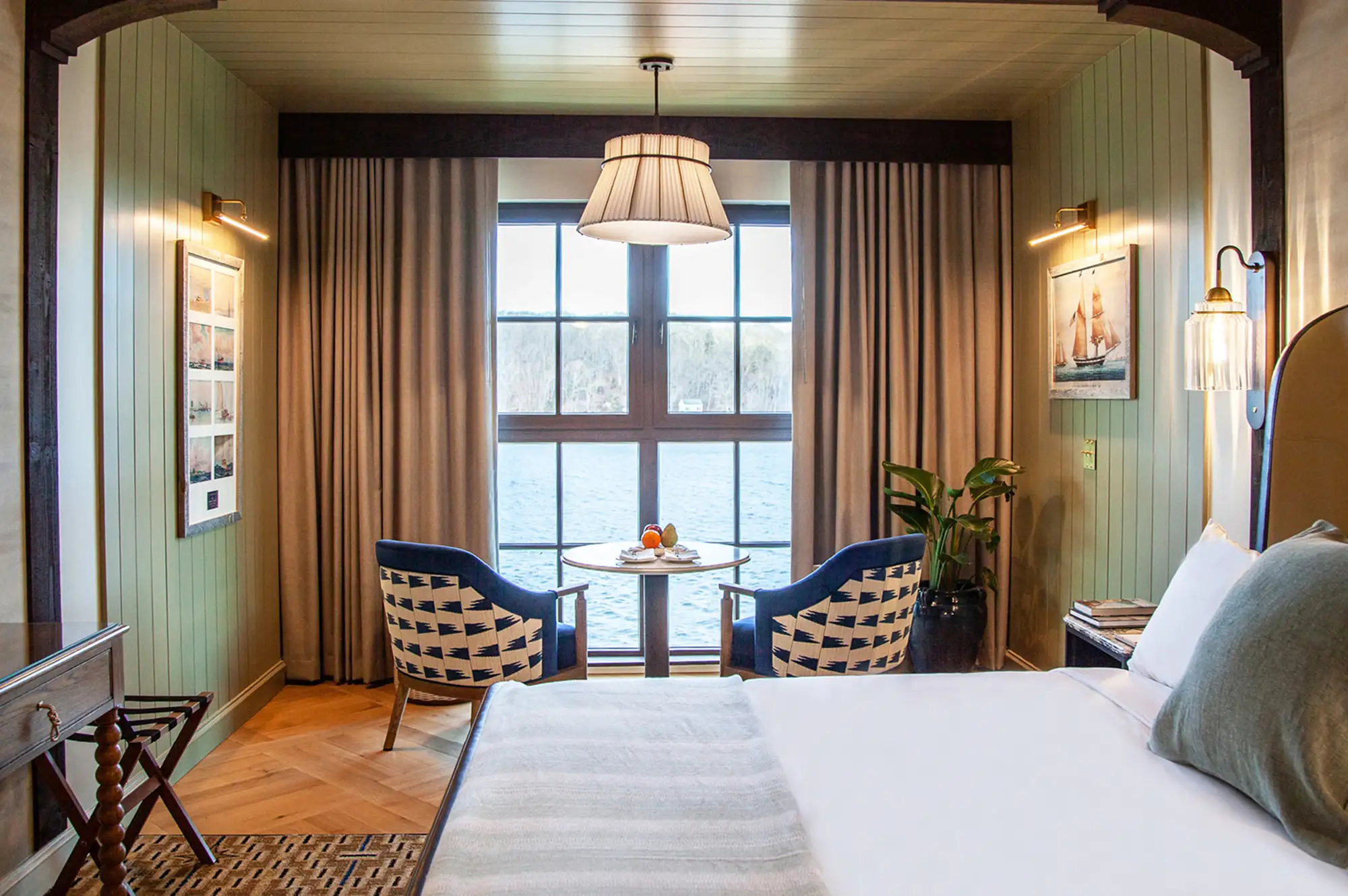 A luxury hotel room at Delamar Mystic featuring contemporary furniture and a large window overlooking the water.