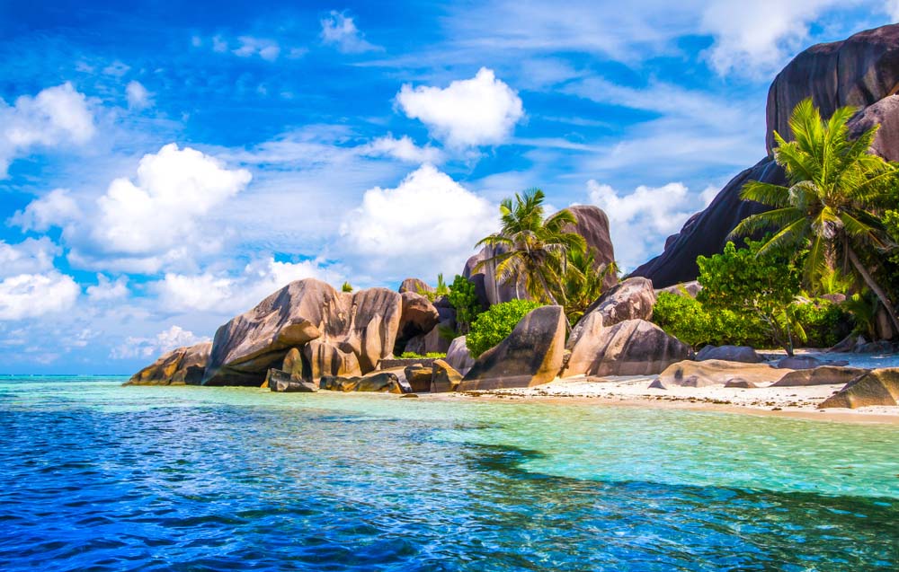 Tropical beach with white sand, turquoise water, and large granite boulders.