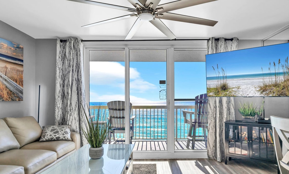A modern living room inside a condo with large sliding glass doors opening to a beach view.