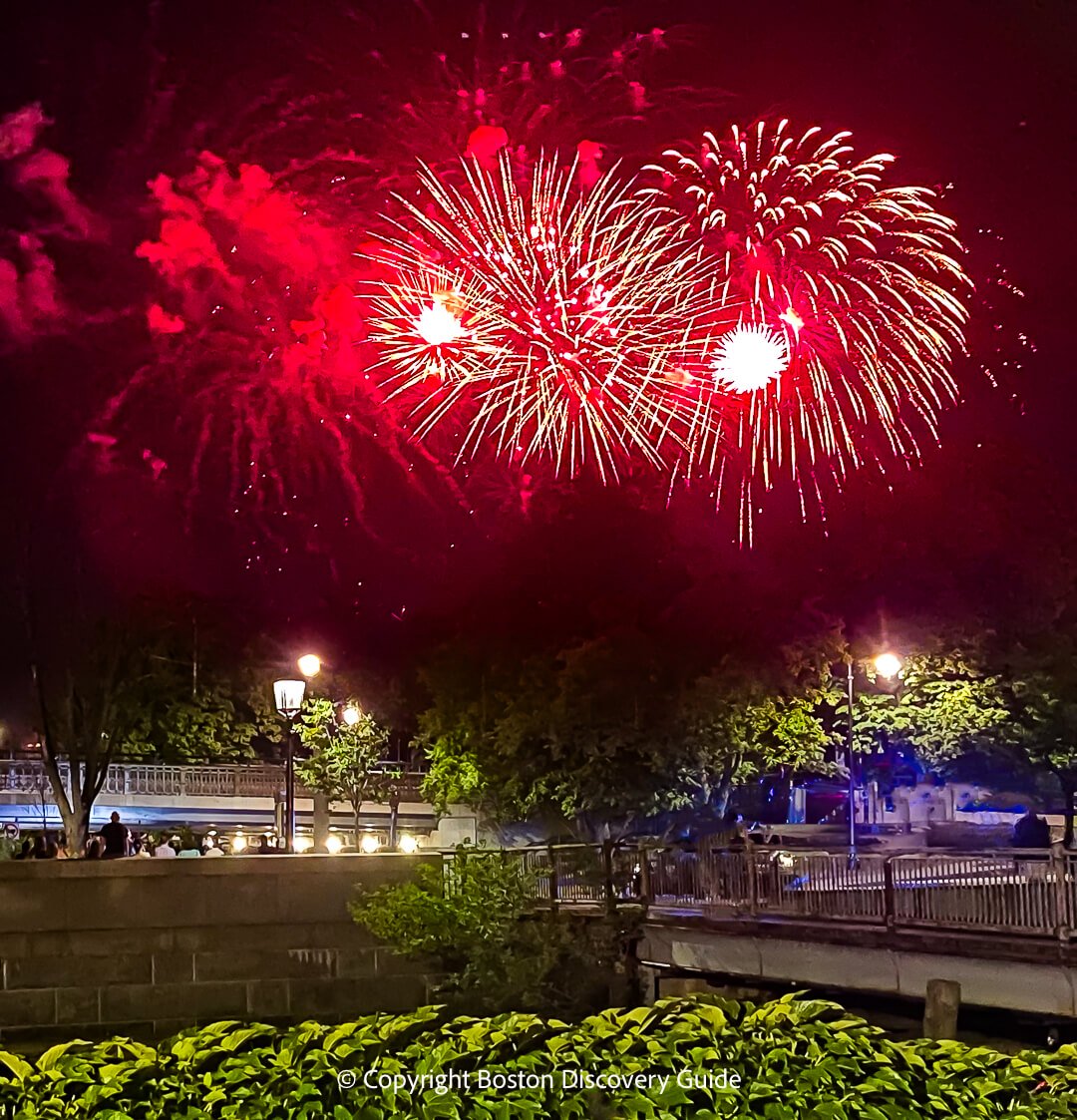 Fireworks exploding over the Charles River with the Longfellow Bridge visible in the background.