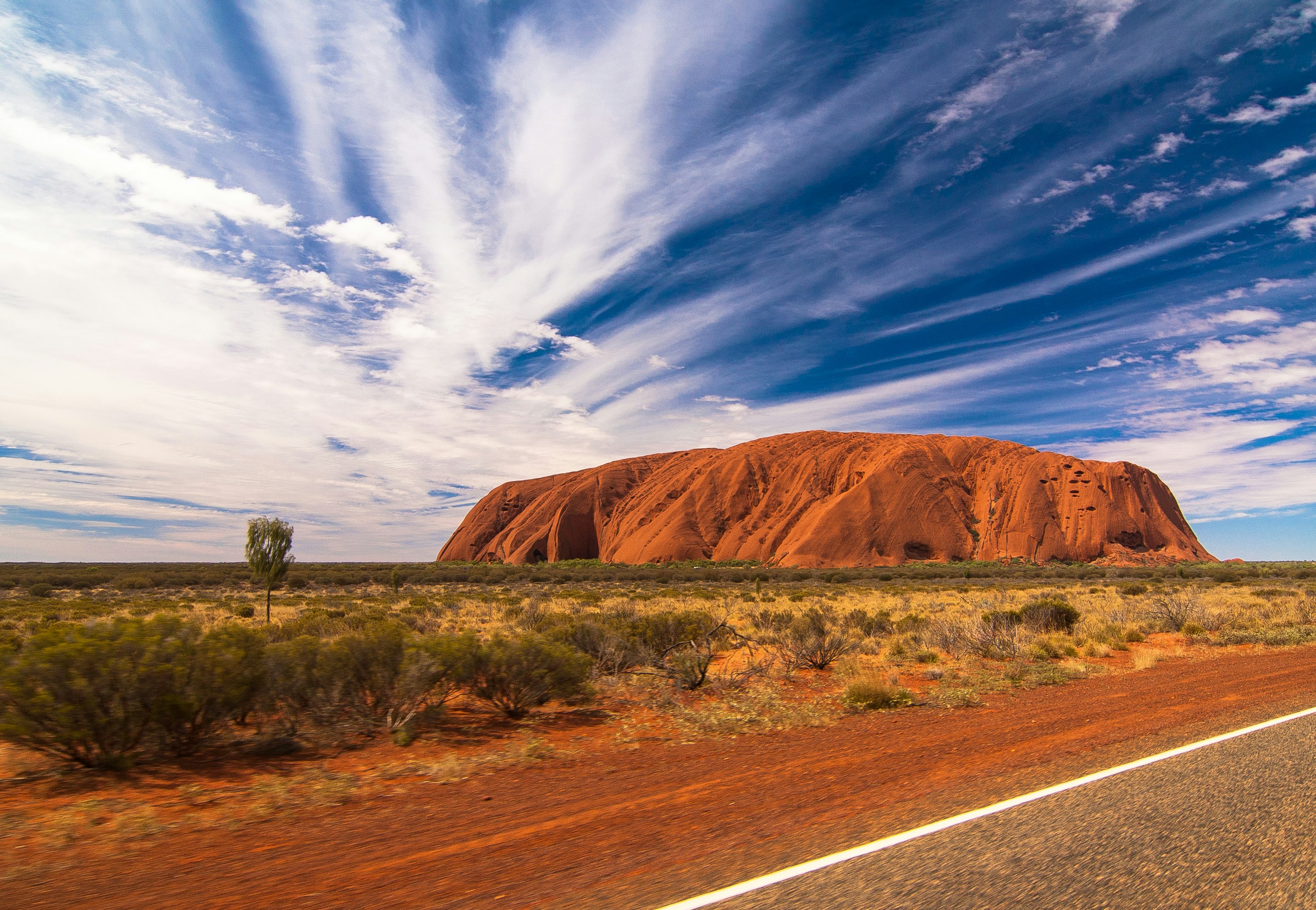 The massive red sandstone monolith of Uluru in the Australian Outback during sunset.
