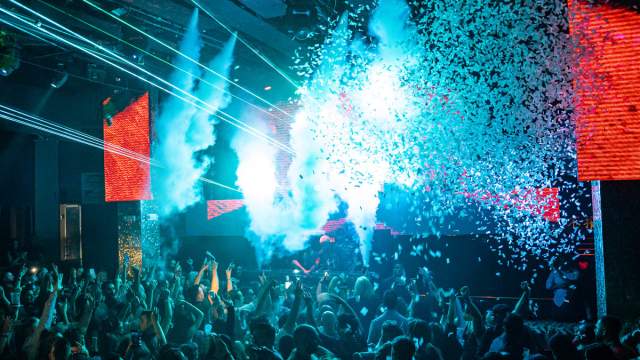 A large crowd of people dancing with their hands up at a brightly lit Las Vegas nightclub.