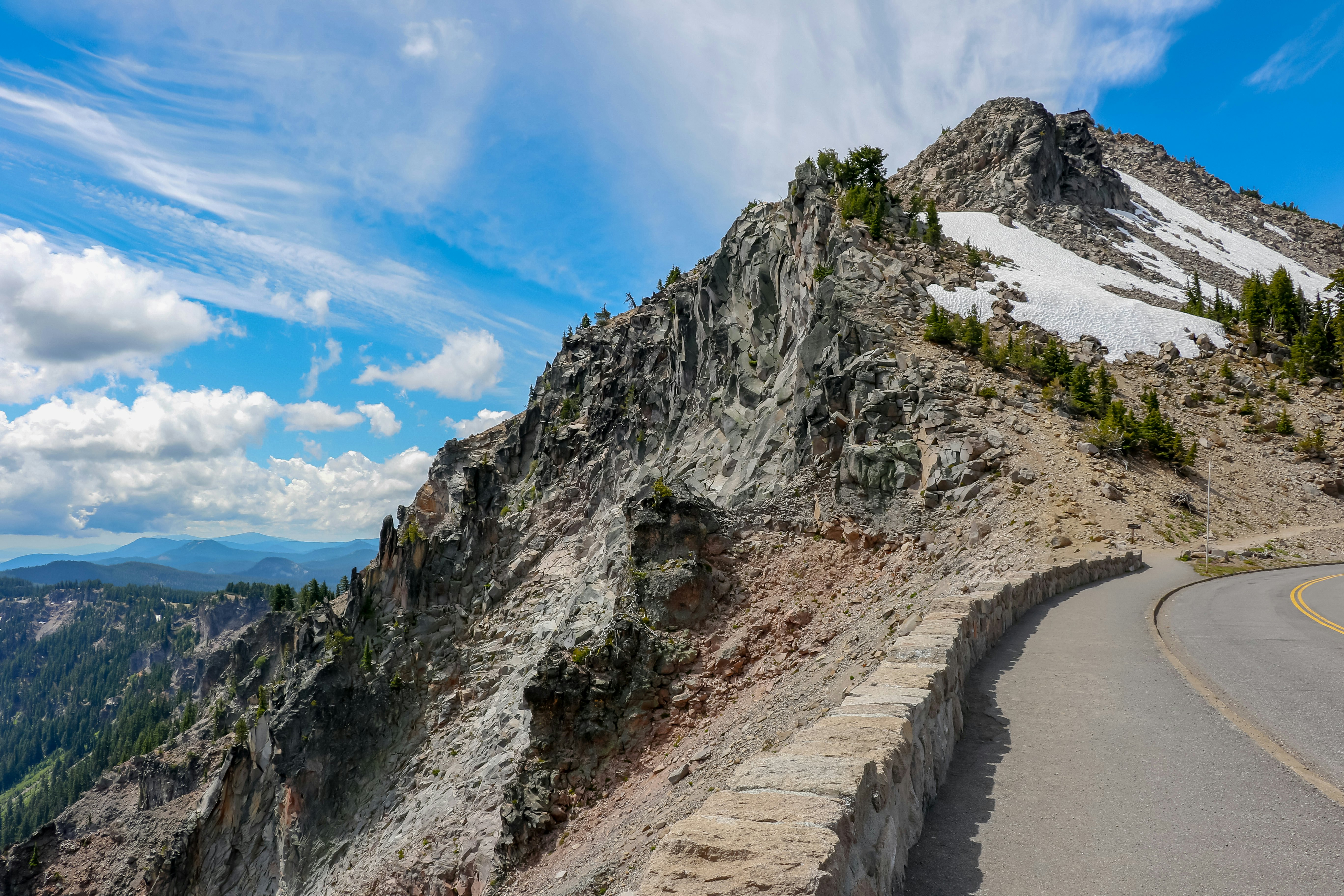 A paved scenic road winding alongside Crater Lake with patches of snow on the surrounding peaks.