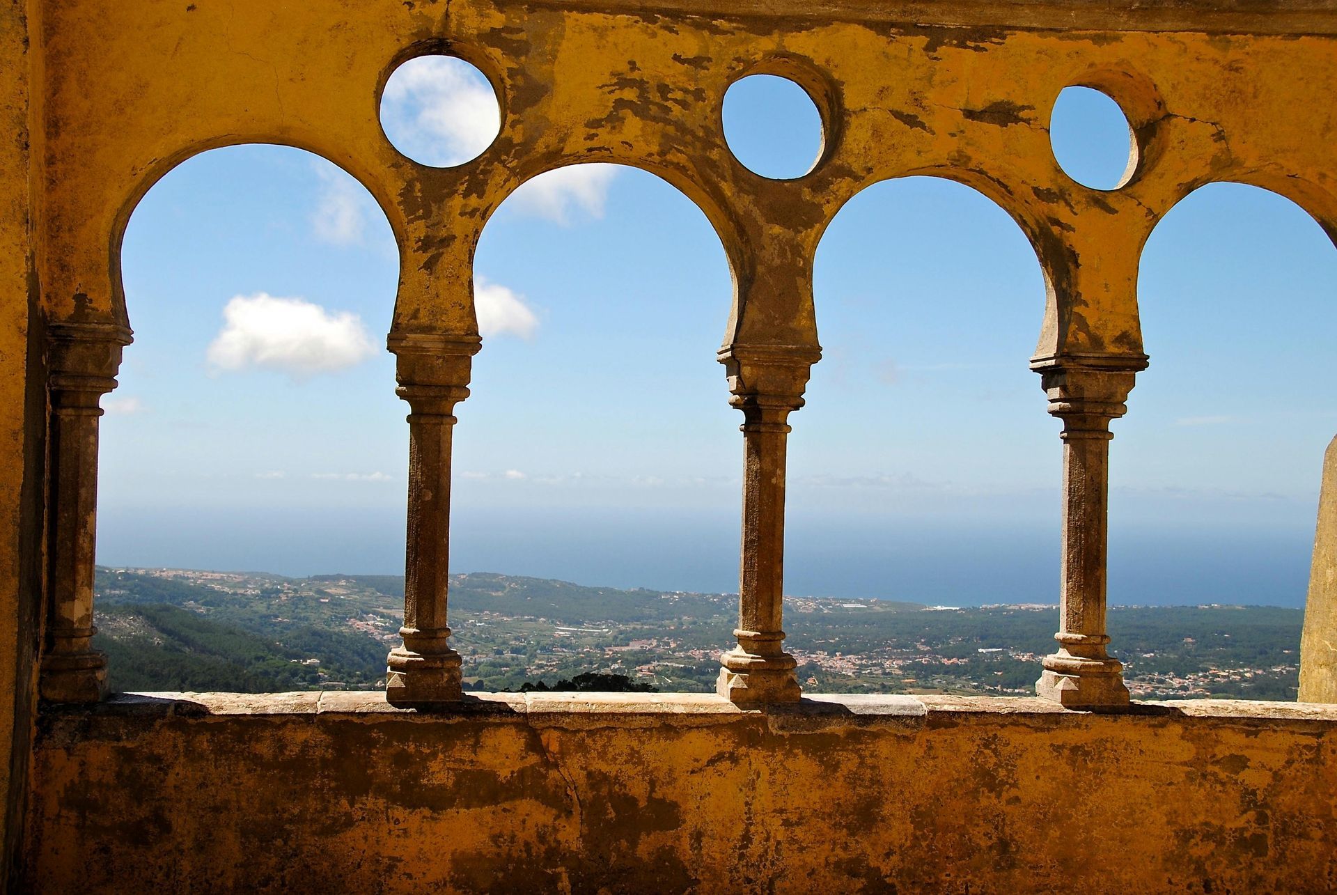A sunny terrace in Portugal featuring yellow classical columns looking out over the blue ocean.