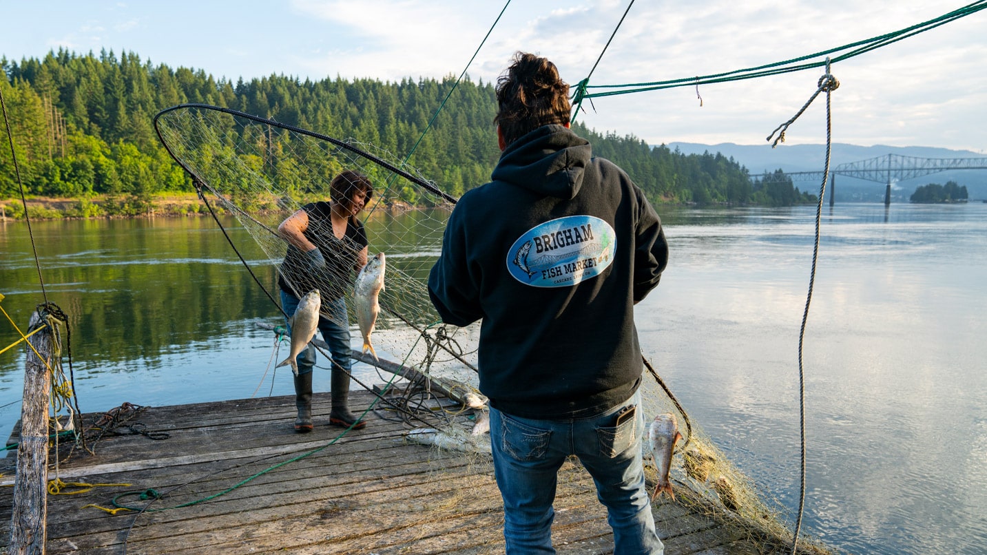 Native women using traditional nets to fish along the banks of a wide river.
