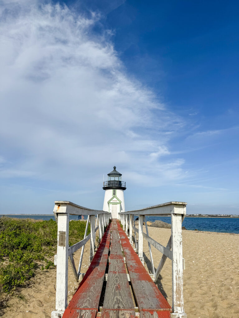 A wide, calm sandy beach at Jetties Beach with light waves and blue sky.