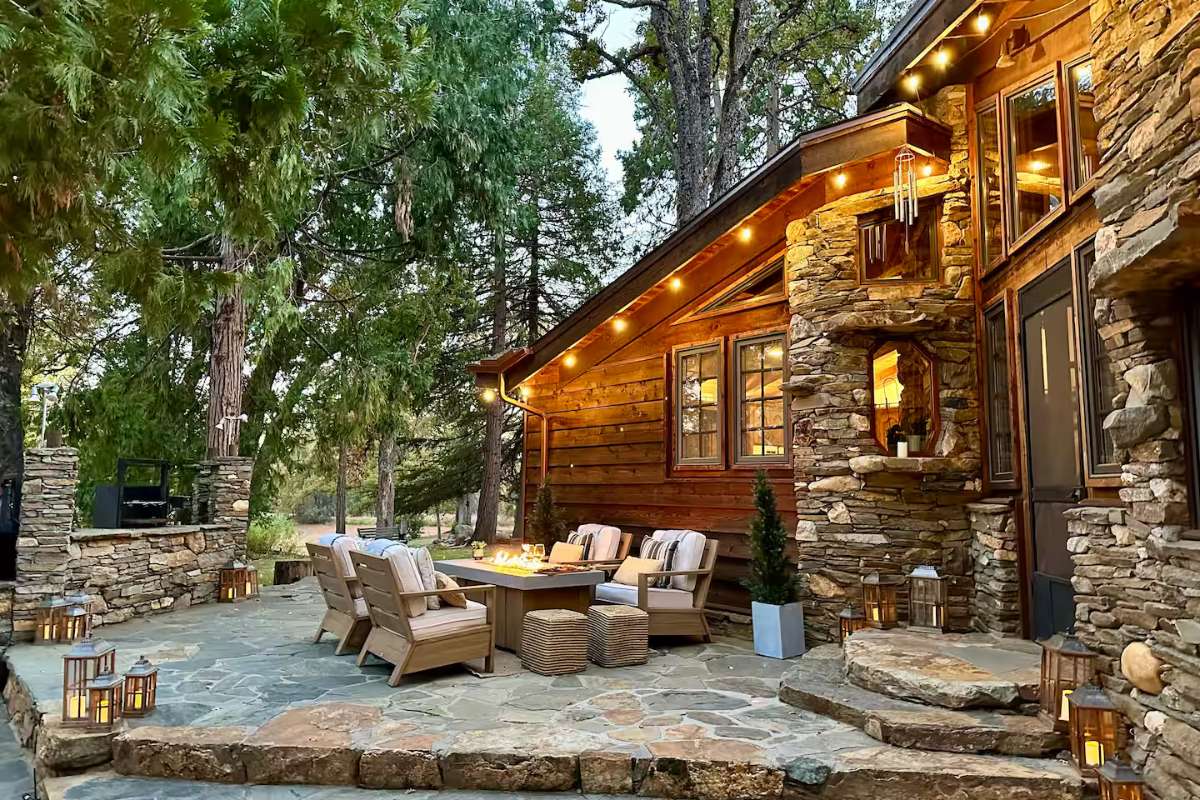 A modern stone house with floor-to-ceiling glass windows surrounded by trees.