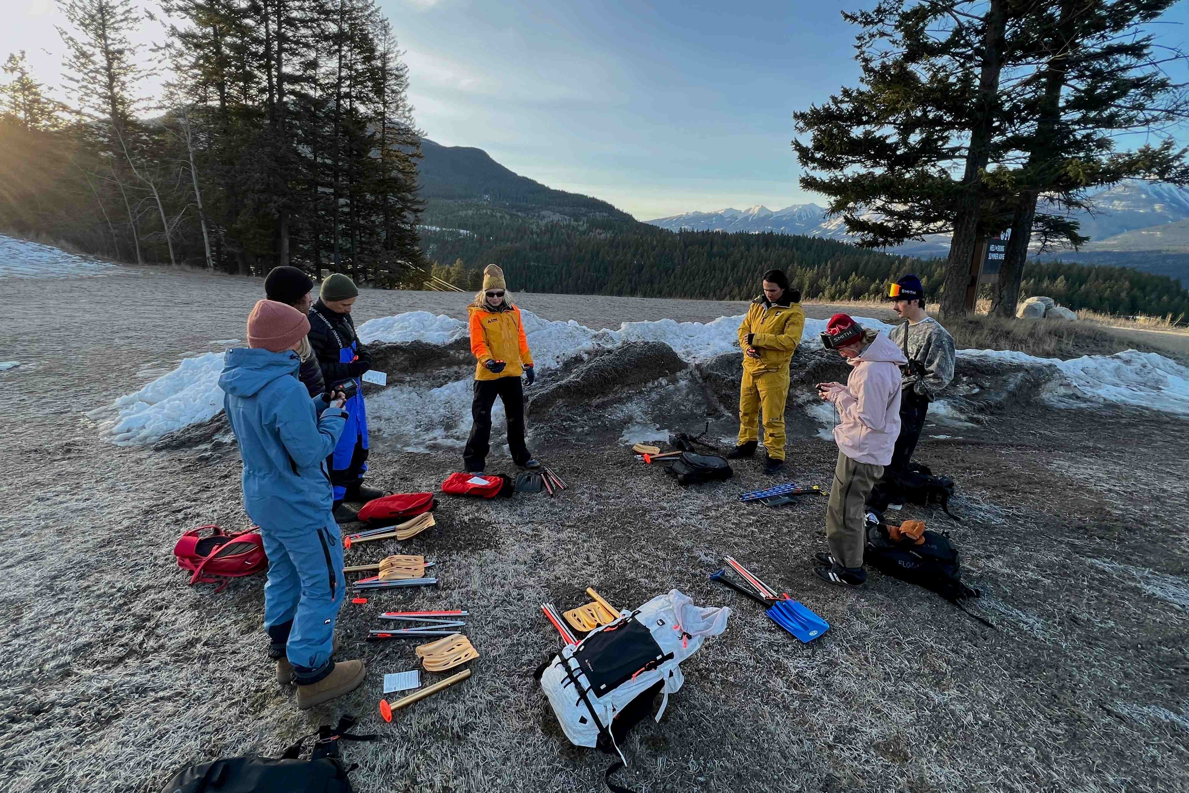 Heli-ski guides showing guests how to use avalanche transceivers and safety gear.