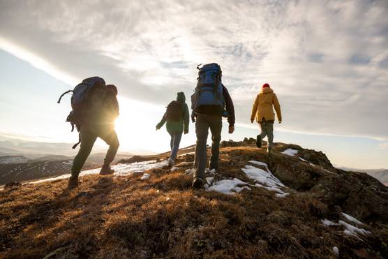 Hikers with backpacks walking along a mountain trail overlooking a scenic valley.